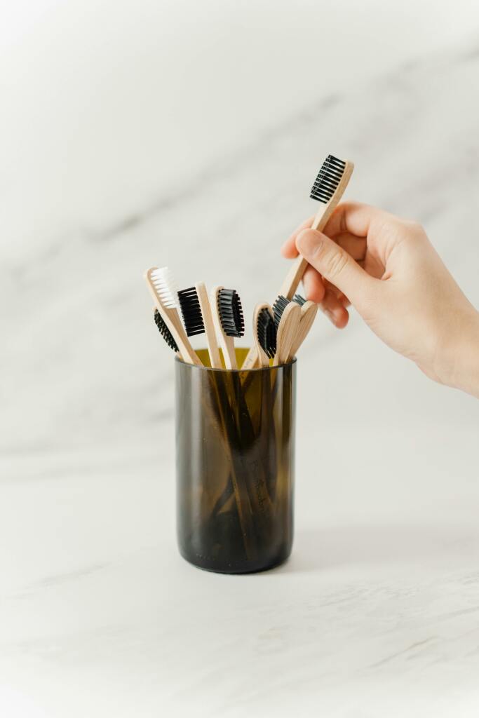Un pot avec plusieurs brosse à dents en bois et une main qui en choisit une.