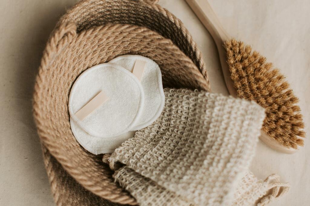 Des lingettes démaquillantes en tissu dans une panière en osier. Une brosse à côté.