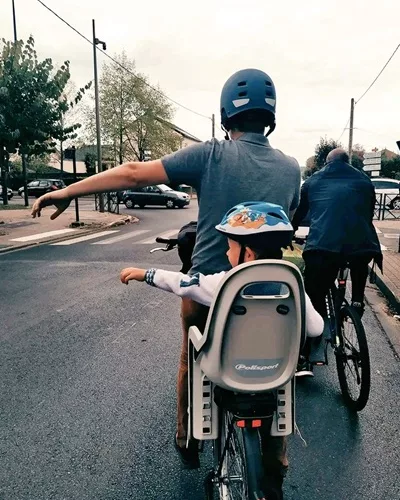 Un papa et son enfant sur un vélo. Ils tendent le bras pour tourner.